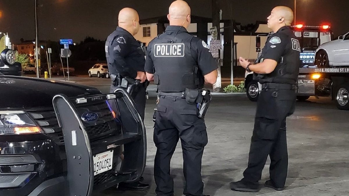 Three uniformed LAPD officers standing near a tow truck